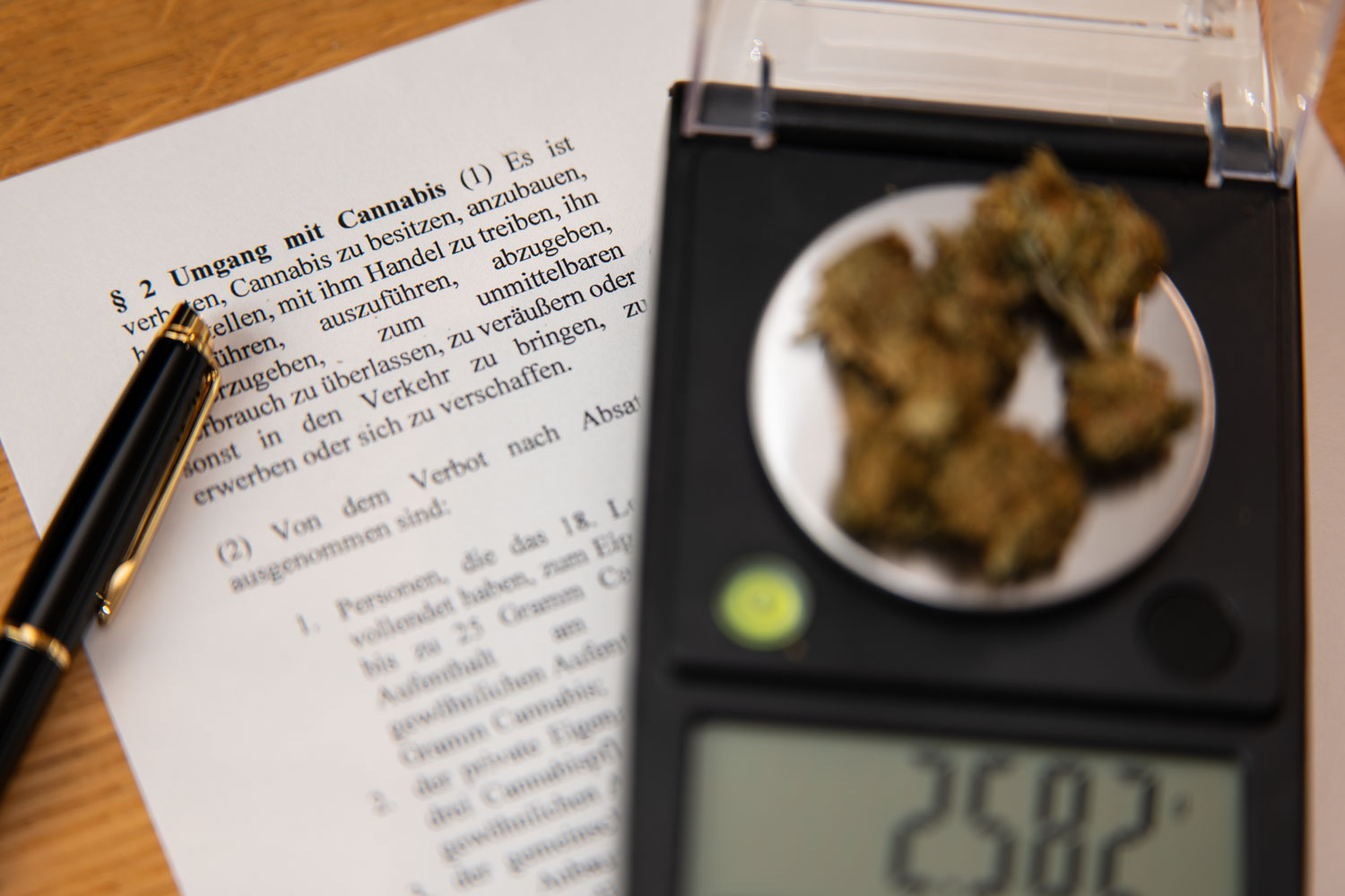 Eine Feinwaage zeigt mit 2,58 Gramm eine völlig legale Menge Cannabis für den Eigenbedarf, daneben liegt ein edler Füller auf dem Text des KCanG.