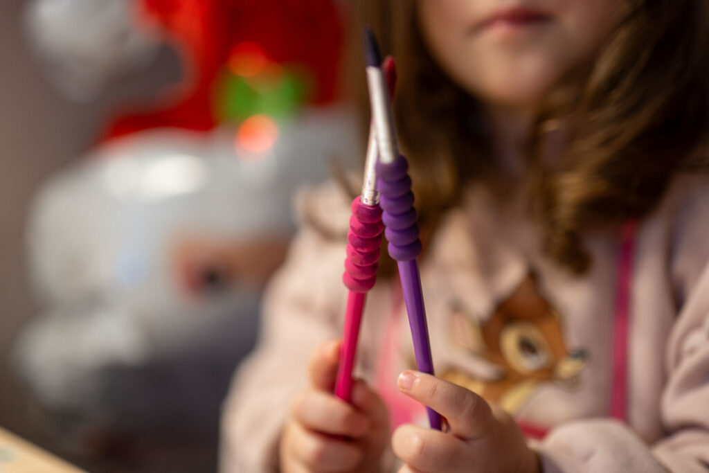 Nahaufnahme der Hände eines kleinen Mädchens, das zwei dicke, bunte Pinsel in Pink und Lila hält, um zu malen.
