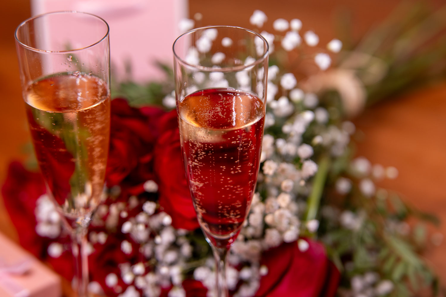 Zwei gefüllte Sektgläser zum Anstoßen bei einem romantischen Date oder Jahrestag vor roten Rosen und einem Geschenk
