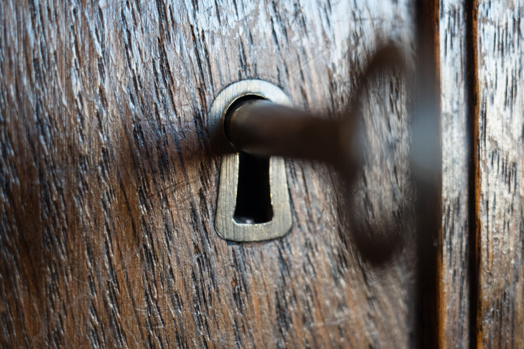 Makroaufnahme eines alten Holzschranks mit eingestecktem, unscharfem Schlüssel im Vordergrund, als Symbolbild für Lösungen, Erfolg und Geheimnisse.