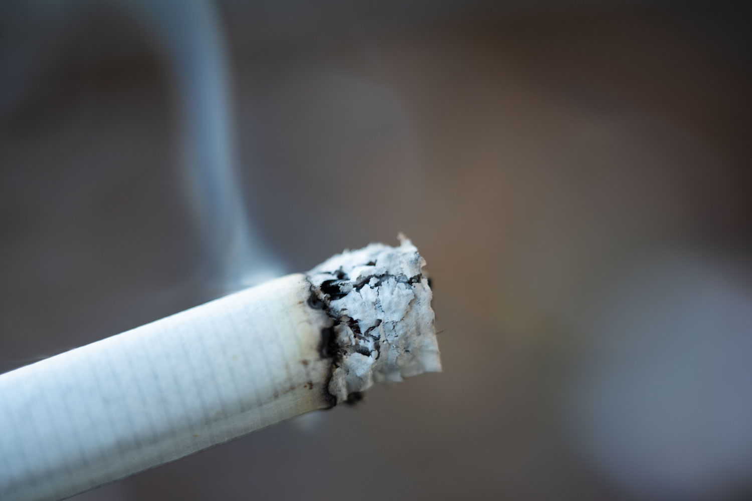 Makroaufnahme einer glimmenden Zigarette mit aufsteigendem Rauch als universelles Symbolbild für Themen wie Raucherentwöhnung, Tabaksteuer und Raucherpausen.